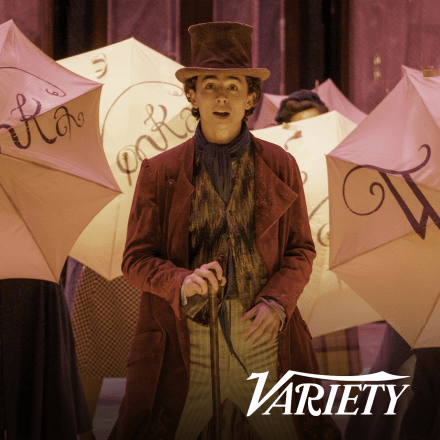 A still from Wonka showing a man wearing a top hat dancing in front of umbrellas saying Wonka.