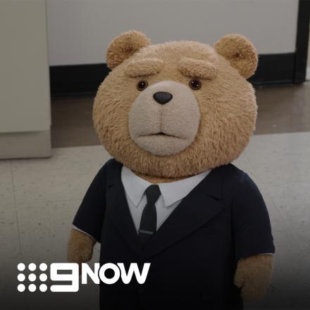 A teddy bear in a suit is in an office setting.