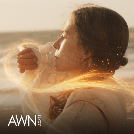 A woman with brown hair creating yellow magic from her hands, with strands of magic coming over her shoulder.