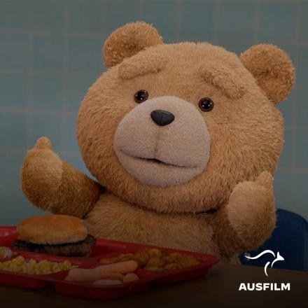 A teddy bear sat at a lunch table with a school lunch giving a thumbs up.