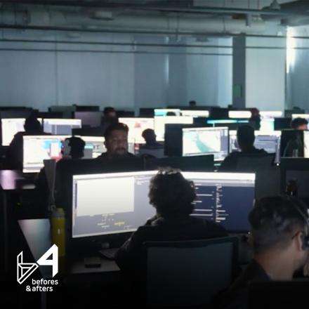 A group of people sat in a room working at computers with double monitors. 