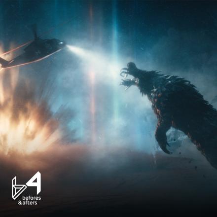 A large scaled monster leaping at a helicopter that is shining a light at it, there is an explosion and blue light in the background. 