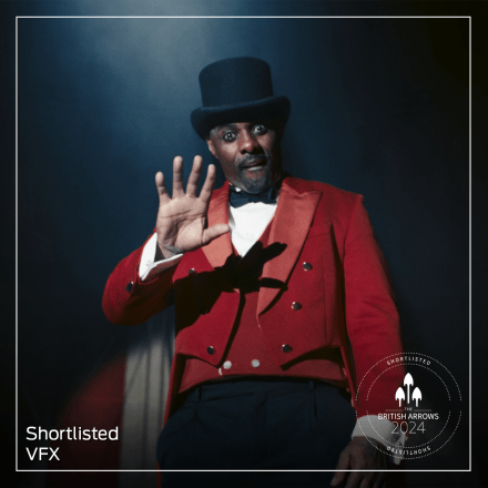 A man in a red coat and black top hat holding up one hand.