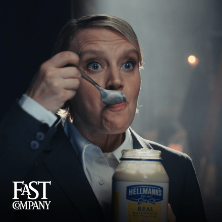 A woman in a suit eating mayonnaise out of a jar with a spoon. 