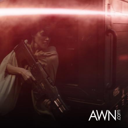 A woman crouched holding a gun as laser gun fire goes over her head. 