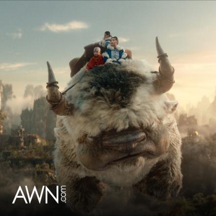 A group of three people sitting on the back of a flying bison-like creature, there is the AWN logo in the bottom left corner.
