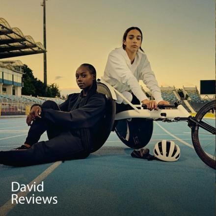 Two para-athletes on a track on sat on the floor and one in a racing wheelchair. 