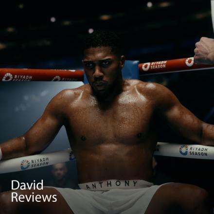A man sitting wearing boxing gloves in the corner of a boxing ring with a CGI crowd behind him.