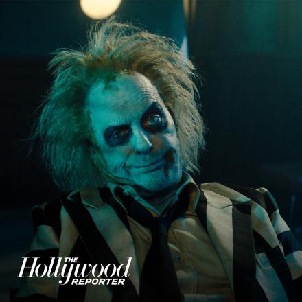 A still of Beetlejuice cast in a green light sitting looking into the camera. 