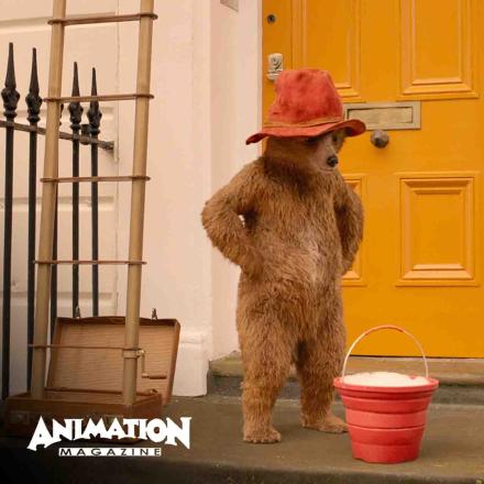 Still of Paddington in Peru film of CG character Paddington looking down at bucket of water and soap. Animation Magazine logo bottom left