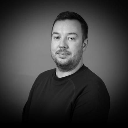 A black and white headshot of a white man against a grey background. 