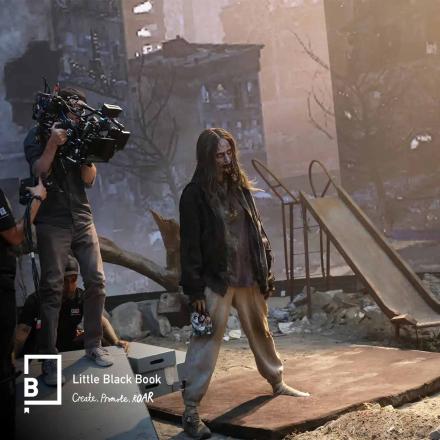 Camera operator films zombie-like actor on post-apocalyptic playground set with rubble and slide during movie production.