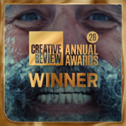 A still from a Columbia Sportware ad showing a man witha. frozen moustache and cracked teeth overlaid with a gold border and a gold Creative Review Logo.