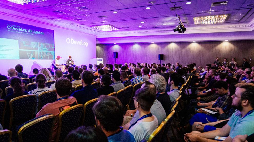 A conference hall full of seated people listening to a talk