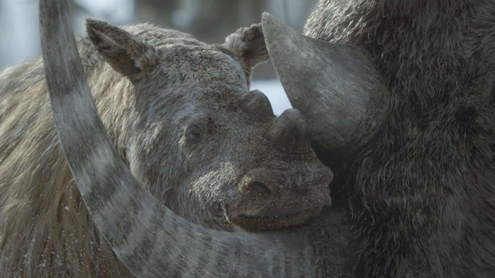A young woolly mammoth, entirely CG animated, nestles into the tusk of its mother