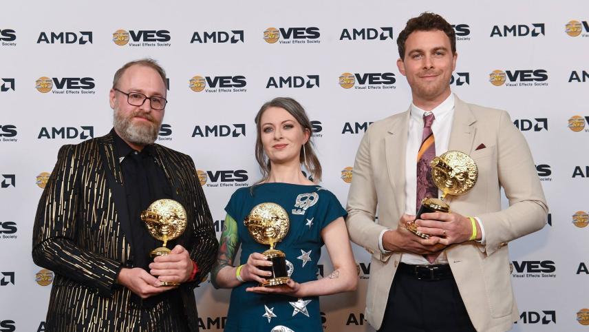 Three people stand on the red carpet at the VES awards, holding golden awards