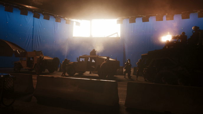 A large tank on a set stage with a large overhead light and a bluescreen in the background.