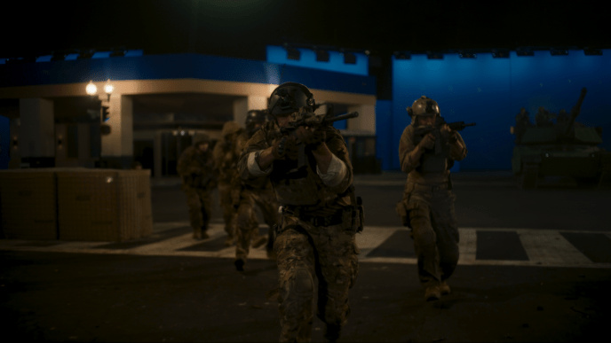 A group of armoured soldiers holding guns walking through a street, there is a bluescreen in the background. 